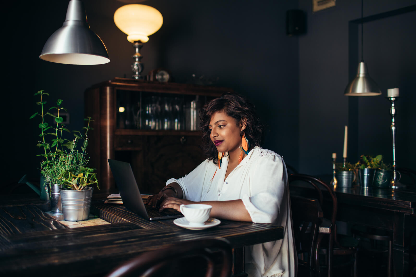 woman sitting alone at a table drinking coffee and working on a laptop