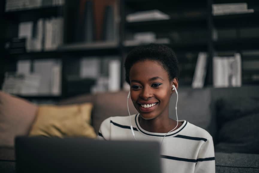woman sitting on couch on laptop with headphones in for online therapy